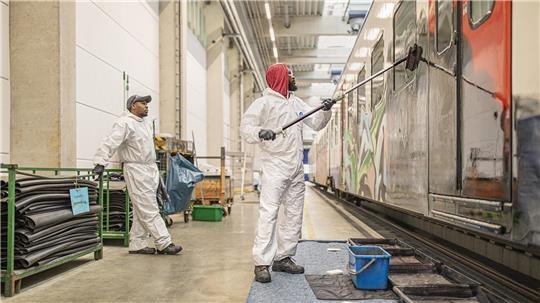 Arbeiter entfernen Graffiti auf einem Triebwagen.
