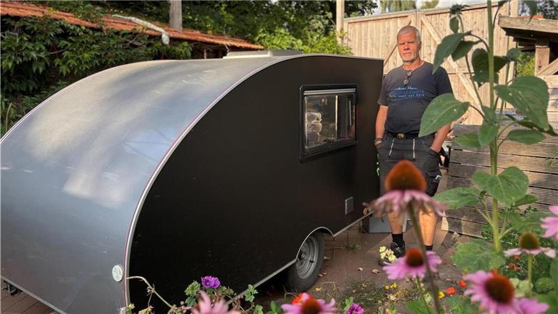 Diese Schneckenhaus-Wohnwagen aus dem Nachbarkreis sind kleine Raumwunder Tischler Harald Prien neben einem dunkelgrauen Mini-Wohnwagen.
