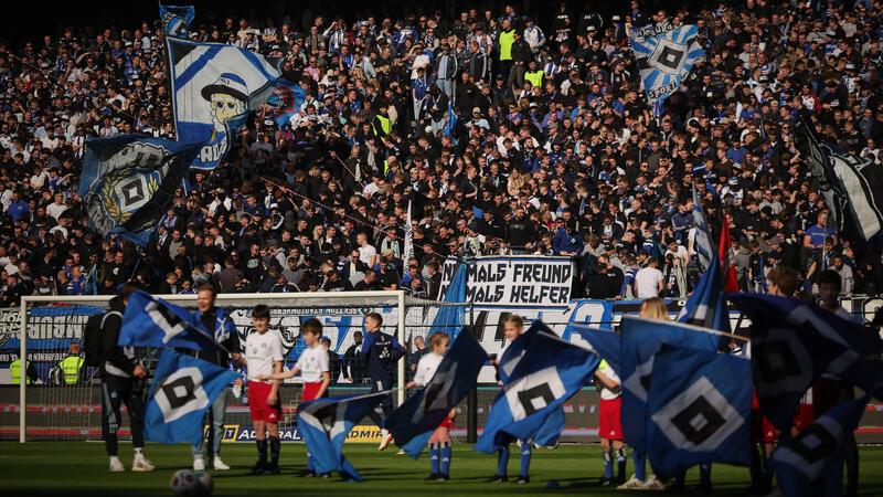 HSV-Fans feiern im Volksparkstadion vor dem Spiel. „Niemals Freund. Niemals Helfer“ ist auf einem Plakat zu lesen.