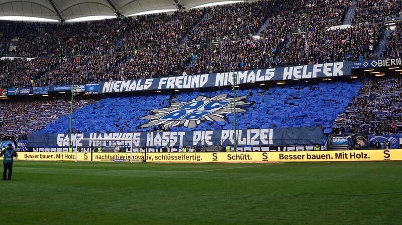HSV-Fans halten Plakate mit der Aufschrift „Niemals Freund, niemals Helfer“ und „Ganz Hamburg hasst die Polizei“ hoch.