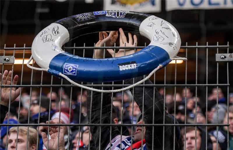 HSV-Fans halten einen Rettungsring in den Vereinsfarben über den Zaun. Foto: Axel Heimken/dpa