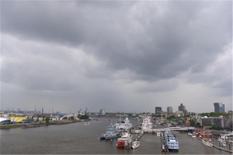 Hamburg: Graue Regenwolken über der Elbe und dem Hafen an der Überseebrücke. Die Elbe hat im Bereich Hamburg wieder mehr Sauerstoff im Wasser, dennoch ist die Situation für die Fische weiterhin angespannt. Foto: Jonas Walzberg/dpa