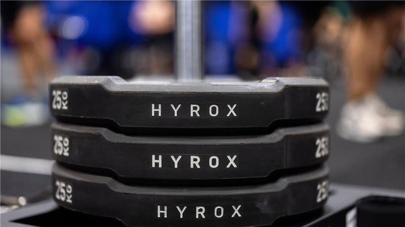 Hantelscheiben mit dem Schriftzug Hyrox an einem Messestand, wo wenig später ein Lauf- und Workout-Wettbewerb stattfinden sollte.
