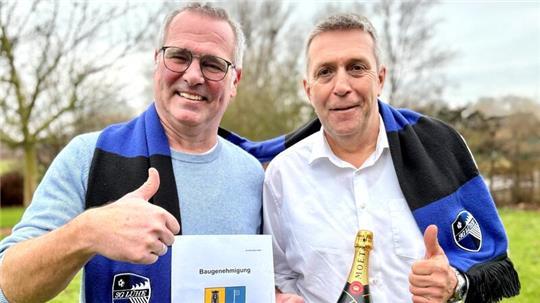 Heiko Baumgarten von der SG Lühe und Samtgemeindebürgermeister Timo Gerke feiern die Baugenehmigung für den Sportplatz Striep in Steinkirchen (von links).