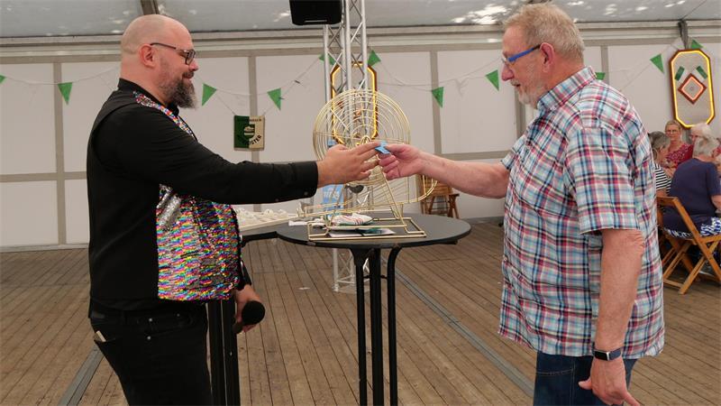 Hein Hoyer hat die erste Bingorunde des Nachmittags gewonnen und bekommt vom Moderator einen Restaurantgutschein überreicht.