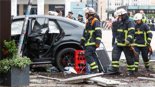 Helfer stehen an einem demolierten Auto vor einer Sparkasse in der Hamburger Innenstadt. 
