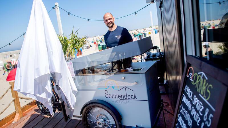 Hendrik Bremer, Betreiber der Milchbude Sonnendeck, baut bei sonnigem Wetter einen Verkaufsstand für Cocktails vor seiner Strandbar auf. Milchbuden haben auf der Nordseeinsel Borkum eine lange Tradition.