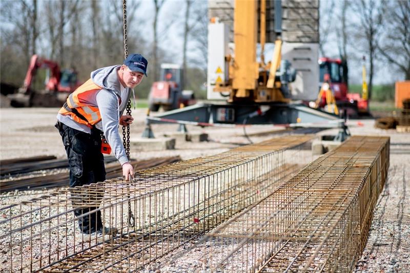 Henry Heidrich, Auszubildender in einem Bauunternehmen, hakt auf einer Baustelle die Eisenkörbe für das Fundament an einem Kranhaken ein. Foto: Hauke-Christian Dittrich/dpa