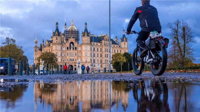 Bilder des Tages Herbstwetter in Norddeutschland: Ein Radfahrer fährt an einer Pfütze vorbei, in der sich das Schweriner Schloss spiegelt.