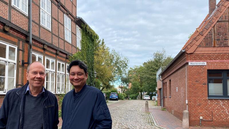 Bernd Utermöhlen und Reiner Sprenger stehen in der Liebfrauenstraße zwischen Stadtbibliothek und Moortorstraße mit dem heutrigen Wehdenhof-Parkplatz im Hintergrund
