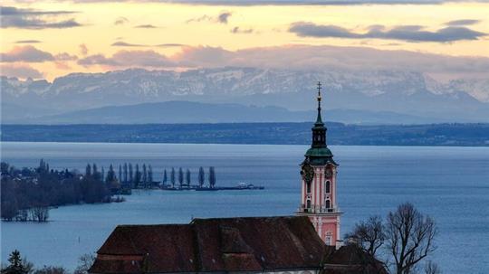 Hinter der ehemaligen Klosterkirche Birnau am Bodensee geht die Sonne auf. Die Alpen sind im Hintergrund zu sehen.