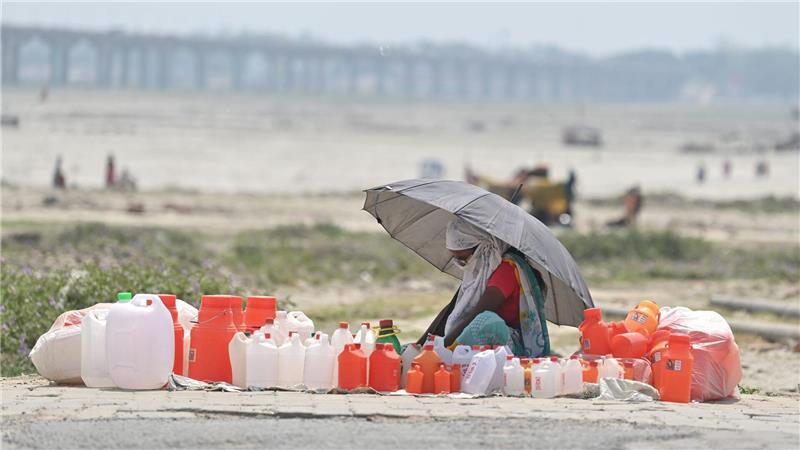 Hitze in Indien: Von Kanistern umgeben wartet ein Verkäufer mit einem Schirm in Prayagraj auf Kunden.