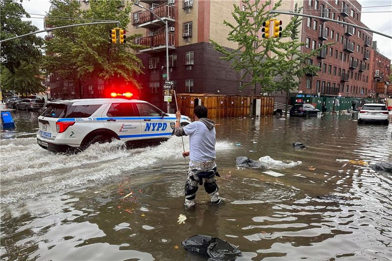 New York versinkt im Regen Hochwasser auf den Straßen von New York: Im Stadtteil Brooklyn versucht ein Mann, mit einem Stock einen Abfluss zu reinigen, während ein Polizeiwagen vorbeifährt.