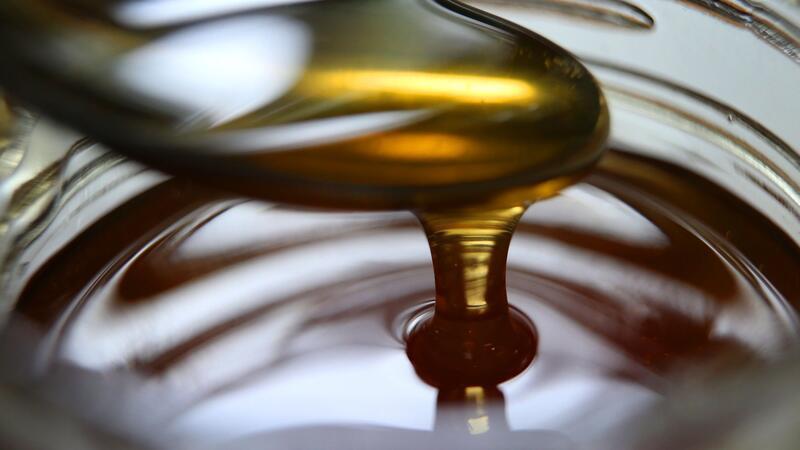 Honig fließt von einem Löffel in ein Honigglas.