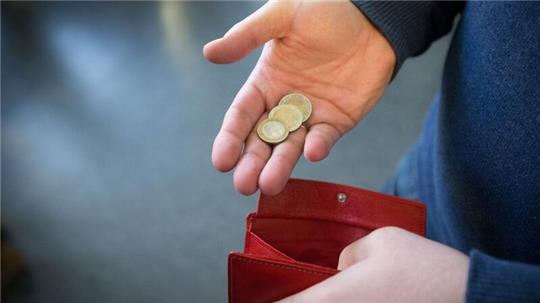 ILLUSTRATIOMünzen im Wert von fünf Euro liegen in einer Hand über einem Portemonnaie.
