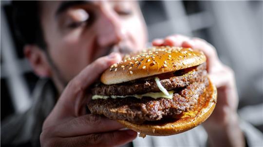 ILLUSTRATION - 18.03.2025, Bremen: ILLUSTRATION - Ein Mann beißt in einen Burger. (zu dpa: «Extrem-Essen: Wenn Trends auf Social Media zur Gefahr werden») Foto: Sina Schuldt/dpa +++ dpa-Bildfunk +++