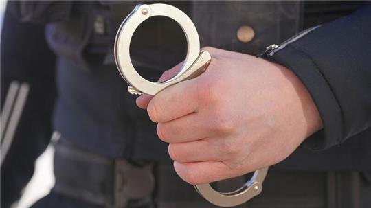 ILLUSTRATION - Ein Polizist hält Handschellen in der Hand.