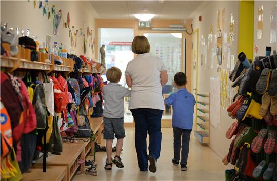 Illustraion: Eine Erzieherin geht mit zwei Kindern über den Flur einer Kita (Symbolbild). Foto: Jan-Philipp Strobel/dpa