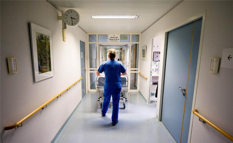 Illustration: Ein Krankenpfleger schiebt ein Krankenbett durch eine Station in einem Krankenhaus. Foto: Daniel Bockwoldt/dpa