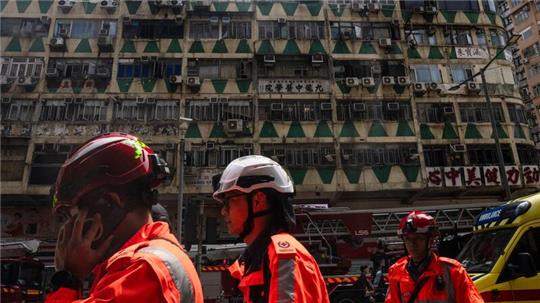 Im Hintergrund ist das ausgebrannte Hochhaus in Hongkong zu sehen - bei der Feuerwehr waren zahlreiche Hilferufe eingegangen.