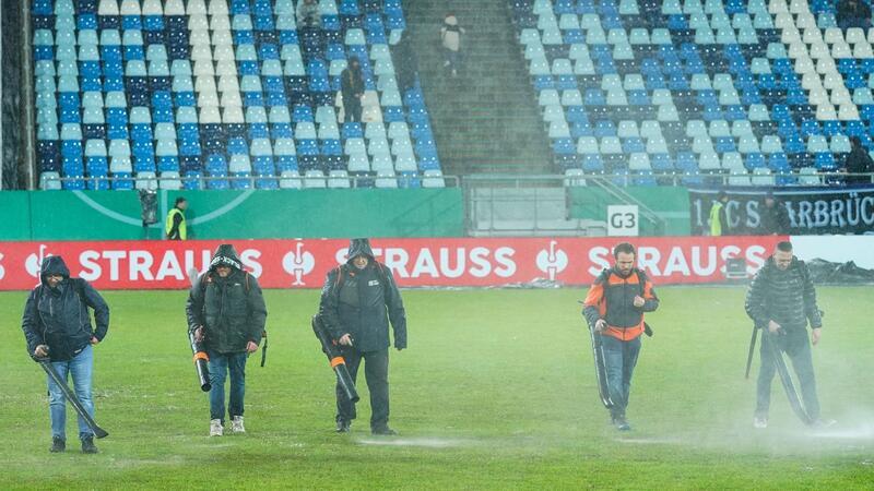Laubbläser reichten nicht: Pokal-Spiel nach Starkregen abgesagt Im Ludwigspark-Stadion versuchen Helfer, Wasserlachen vom Spielfeld zu entfernen.