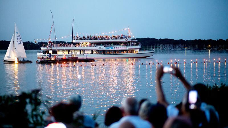 Im Rahmen der Lichternacht verwandelt sich der Kurpark in Bad Zwischenahn in ein Farbenmeer. Zahlreiche Besucher schauen Schwimmerinnen und Schwimmern zu, die mit brennenden Fackeln im Wasser schwimmen.