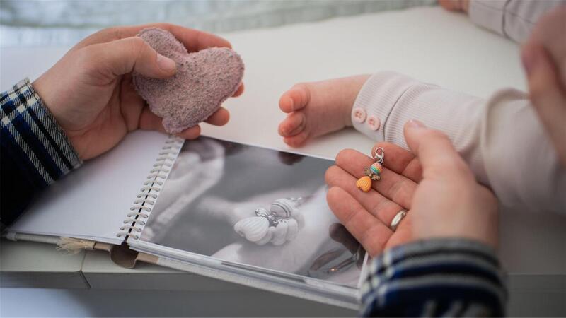 In Erinnerung an ihr „Sternenkind“ Trude, bewahren Björn und Nora Lenkeit liebevolle Fotos mit ihrer verstorbenen ersten Tochter auf, auch das kleine Stoffherz und der Glasperlen-Engel sind ihnen kostbare Erinnerungsschätze.