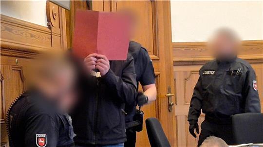 In Handschellen und begleitet von mehreren Justizbeamten wird der Angeklagte in den Gerichtssaal geführt.