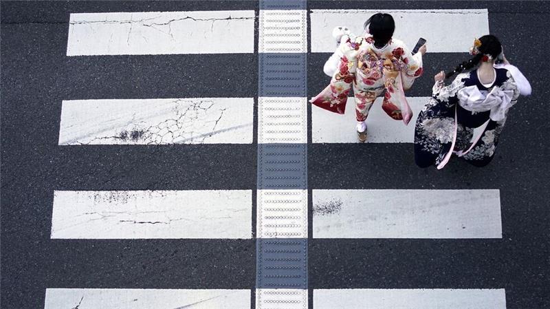 In Kimono gekleidete Frauen gehen über einen Fußgängerüberweg, um den Tag der Volljährigkeit zu feiern.