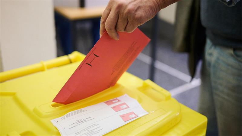 Eine Umschlag wird in eine Wahlurne gesteckt.