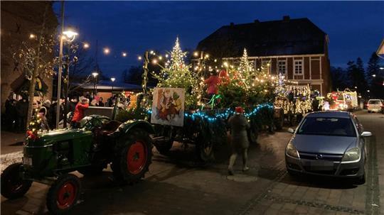 In der Gemeinde Drochtersen kommen der Weihnachtsmann und seine Engel und Wichtel auf einem lichtergeschmückten Trecker mit Anhänger.