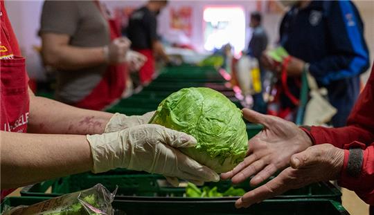 In der Laib und Seele- Ausgabestelle in Berlin verteilt eine ehrenamtliche Mitarbeiterin einen Eisberg Salat. Foto: Christophe Gateau/dpa