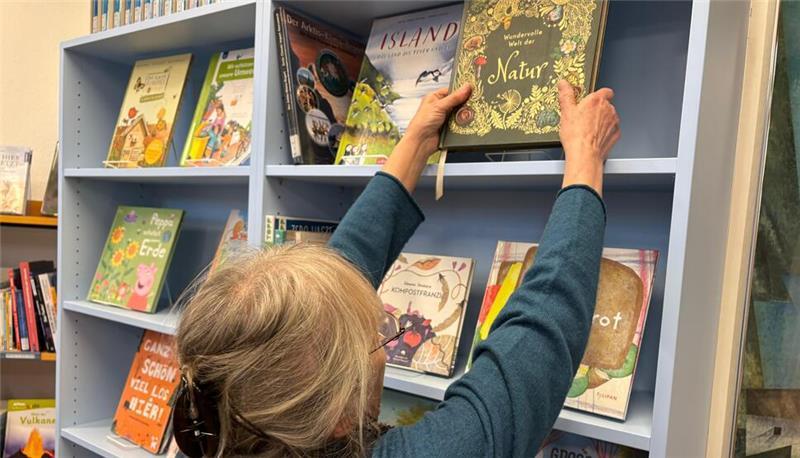 In einer Bücherwand reiht die Büchereileiterin die beliebten Kinderbücher auf.