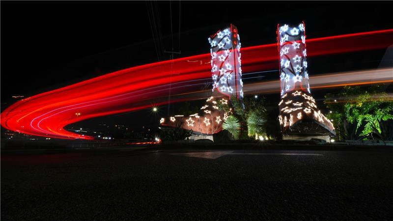 In einer Langzeitbelichtung fahren Fahrzeuge an einem Paar Cowboystiefel vorbei, die 40 Fuß hoch und 30 Fuß lang sind und für die Feiertage mit Lichtern geschmückt wurden.