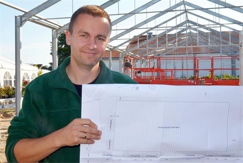Inhaber Klaus Tobaben hält den Bauplan hoch. Im Moment wird der hintere Teil des neuen Gartencenters gebaut. Der vordere Teil soll im nächsten Spätsommer an der Reihe sein. Dann wird sich alles zu einem kompakten Gebäudekomplex zusammenfüge