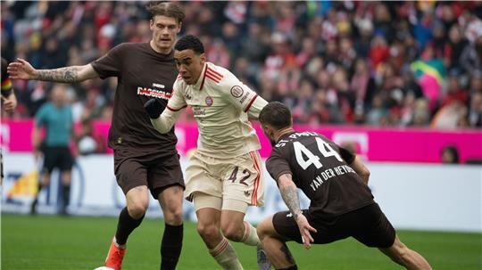 Jamal Musiala (M) vom FC Bayern München, Siebe Van der Heyden (r) vom FC St. Pauli und Eric Smith vom FC St. Pauli kämpfen um den Ball.
