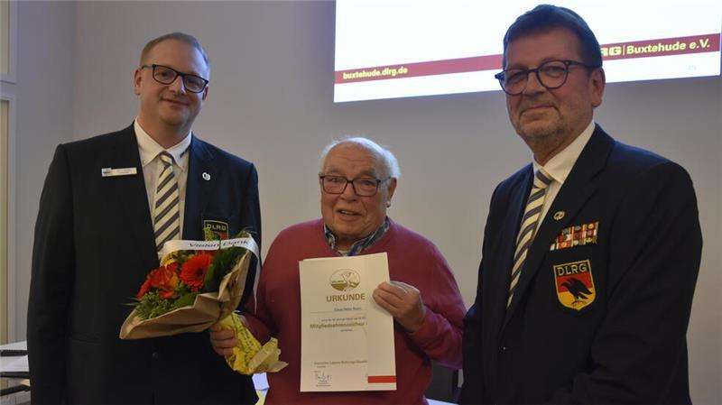 Jan Blanke (links) und Rainer Bohmbach überreichen Claus Dieter Rosin die Ehrenurkunde für 60 Jahre Mitgliedschaft in der DLRG.