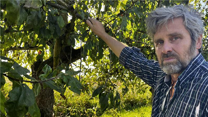 Jan Witt im Apfelhof. Das Blattwerk der Bäume verdeckt die Schornsteine der Industrie am Horizont.