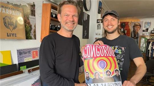 Jan iso Jürgens (links) und René Biernath halten ein Konzertplakat von Congoroo in die Kamera.