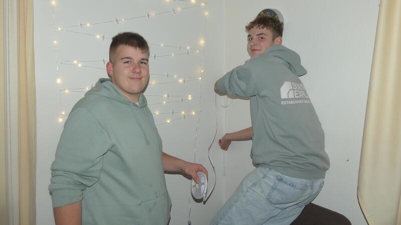 Jason (links) und Lauren sind mit Feuereifer dabei, LED-Streifen an den Wänden des Jugendtreffs anzubringen, die für eine stimmungsvollere Beleuchtung sorgen sollen.