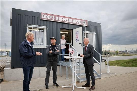 Jens Meier (von links), Geschäftsführer HPA, Odo Wehr, Gastronom, und Peter Tschentscher (SPD), Bürgermeister, unterhalten sich vor Odo’s Kaffeeklappe im Hafen Steinwerder. Foto: Charisius/dpa