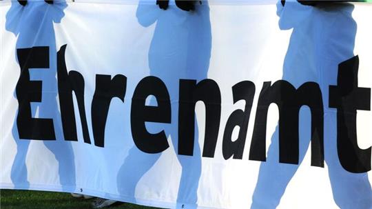 Jugendliche halten vor einem Fußball-Bundesligaspiel ein Banner mit der Aufschrift „Ehrenamt“ in den Händen.