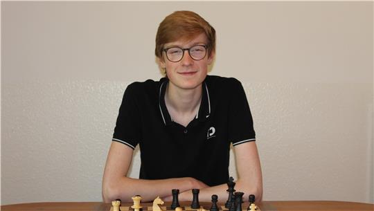 Justus Ibe sitzt am Tisch, vor ihm steht ein Schachbrett mit -figuren.