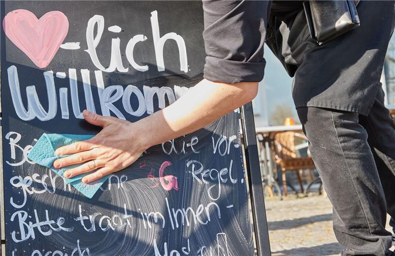 Kellner Tonet Devolli vom Restaurant Mühlstein in Wedel beseitigt die Hinweise zu den 3G-Regeln.