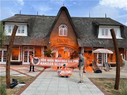 Klima-Aktivisten haben sich vor einem besprühten Luxusgeschäft auf der Insel Sylt platziert. Foto: Julius-Christian Schreiner/dpa