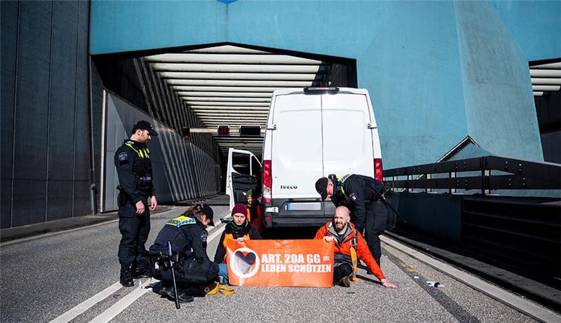 Klimaaktivisten bringen Autoverkehr durch Hamburg zum Erliegen Klimaaktivisten haben sich auf der Fahrbahn der Autobahn 7 festgeklebt und blockieren so die Zufahrt des Elbtunnels in Richtung Norden. Foto: Daniel Bockwoldt/dpa