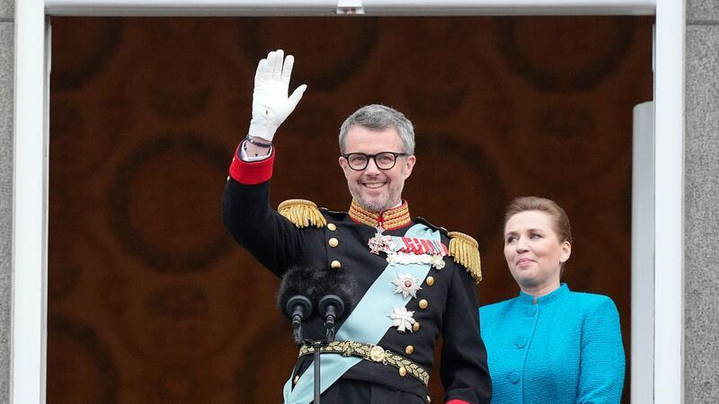 König Frederik X. von Dänemark winkt vom Balkon des Schlosses Christiansborg, während die dänische Ministerpräsidentin Mette Frederiksen zusieht.