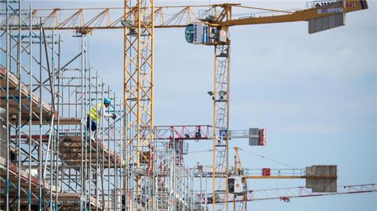 Kräne und ein Arbeiter auf einer Hochbaustelle. Dieser Wirtschaftszweig leidet momentan besonders.