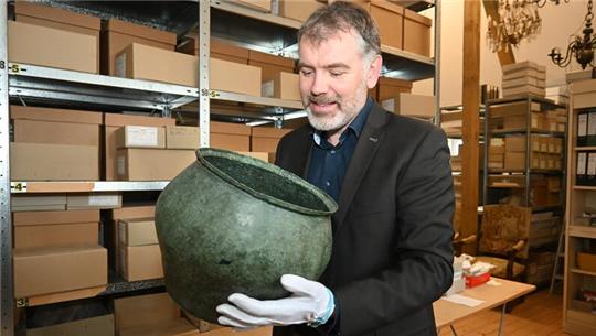 Kreisarchäologe Daniel Nösler blickt in eine Urne aus Apensen: In dem vor 1900 Jahren gefertigten gallorömischen Bronzegefäß mischten die Römer einst ihren Wein mit Gewürzen.