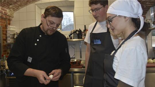 Küchenchef Thomas Kupfer (links) erklärt Mattis Franzke und Festina Rama, wie Pilze tourniert werden.